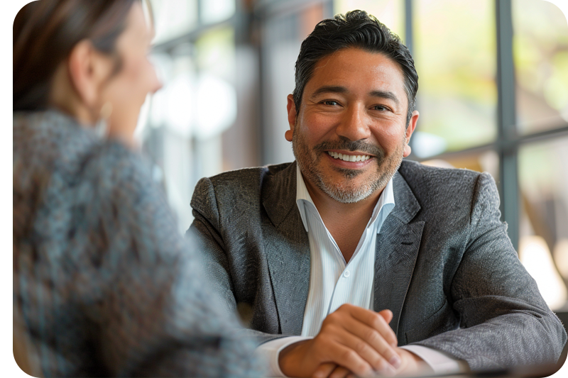 Hispanic man, wearing a blazer and white shirt, smiling and attending a meeting with a female client in a suit